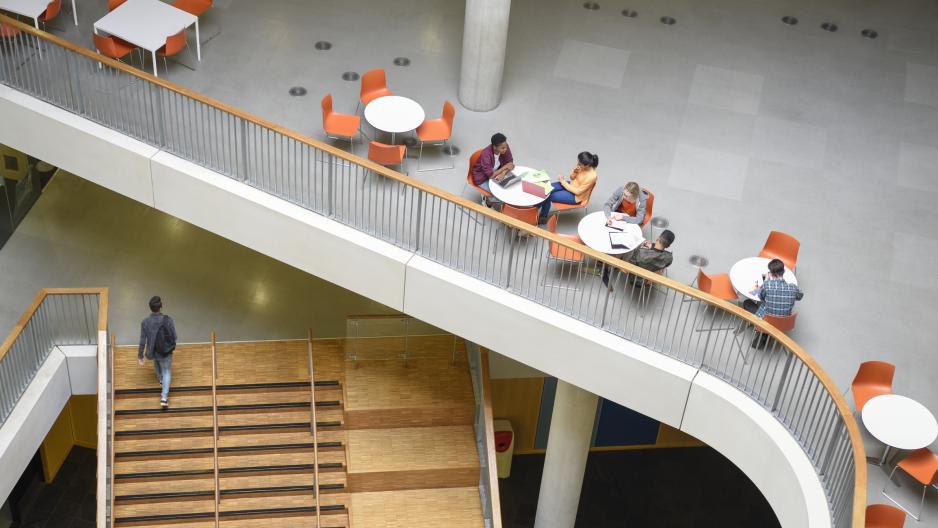 Oversiktsbilde av flere studenter eller forskere som sitter og jobber i grupper og en mann som går opp en trapp