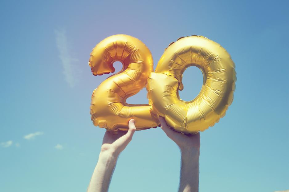 20-tall står med gullballonger mot blå himmel