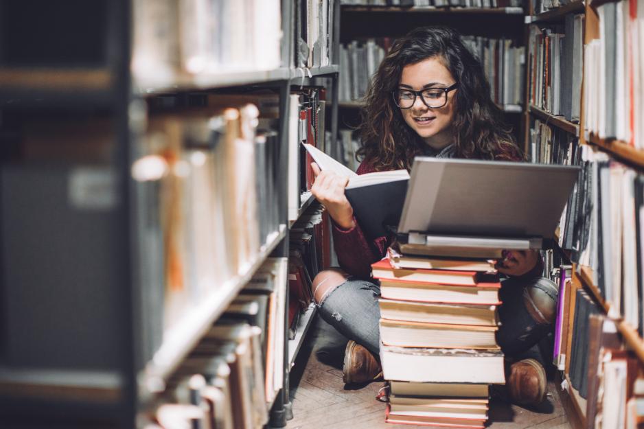 En kvinne sitter på gulvet i et bibliotek og leser bøker.