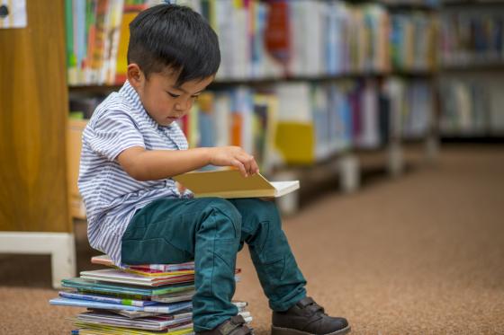 Liten gutt som sitter på en bokstabel og leser 