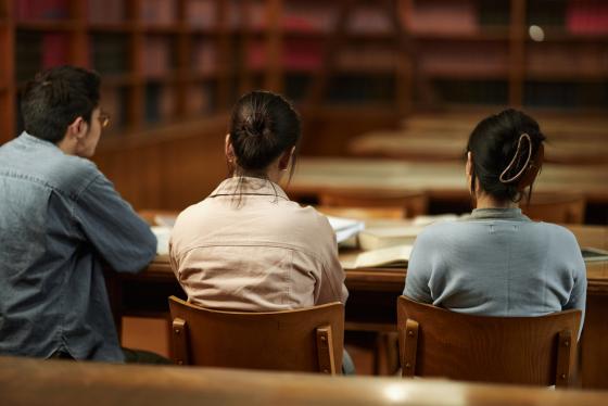 Tre studenter sitter sammen i et bibliotek på campus. 