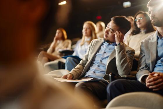 En mann sitter med lukkede øyne i et auditorium sammen med mange andre mennesker