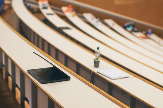 Én laptop på pulten blant mange tomme pulter i et tomt auditorium på universitetet
