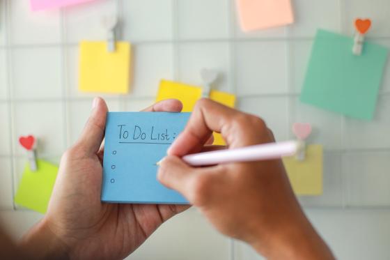 Bilde av hender som skriver to to-liste og henger opp post it-lapper