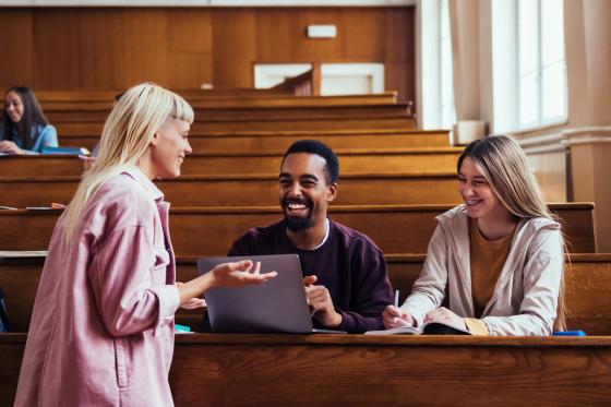 Tre studenter sitter i et auditorium og diskuterer smilende