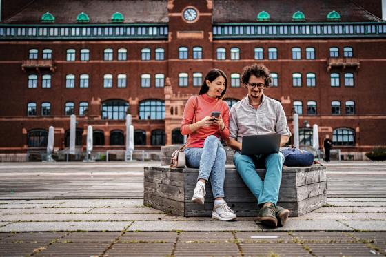 En ung kvinne og en ung mann sitter p&aring; en benk i en storby