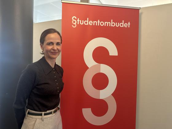 Studentombud Marianne H&oslash;va Rustberggard st&aring;r foran en plakat der det st&aring;r &laquo;Studentombudet&raquo;