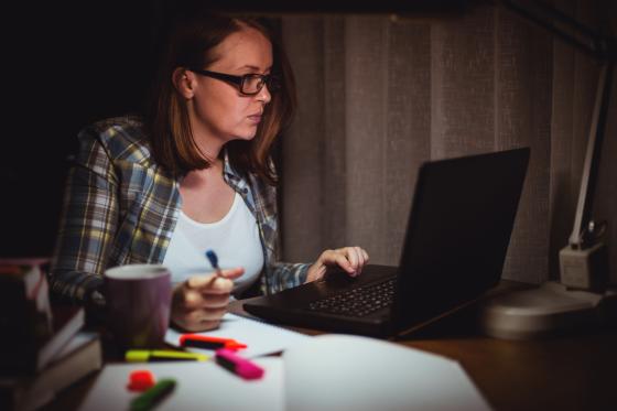 Ung, sliten kvinne jobber sent og sitter ved pc-en hjemmefra 