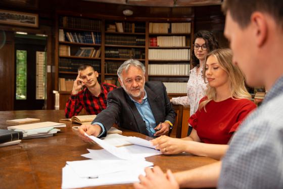 Mannlig professor sitter ved et bord og underviser en gruppe studenter