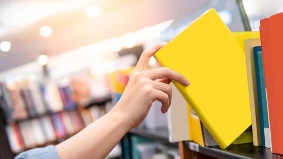 En person tar ut en gul mappe fra en bokhylle.