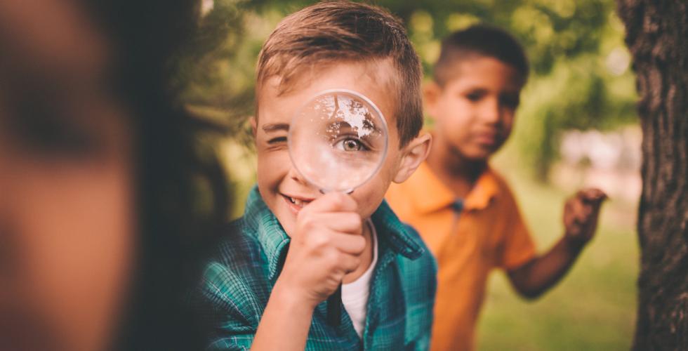 Boy in park holding a magnifying glass to his eye.