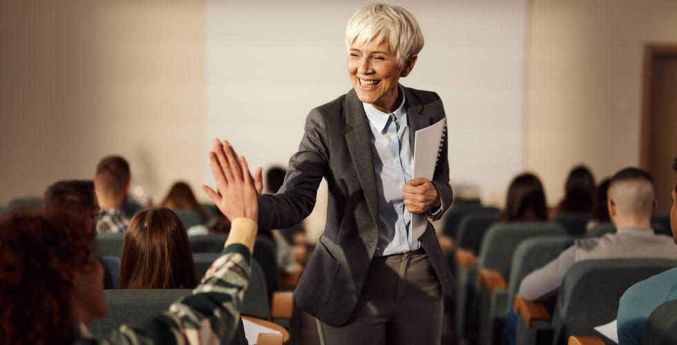 Smilende kvinnelig professor gir high-five i et auditorium