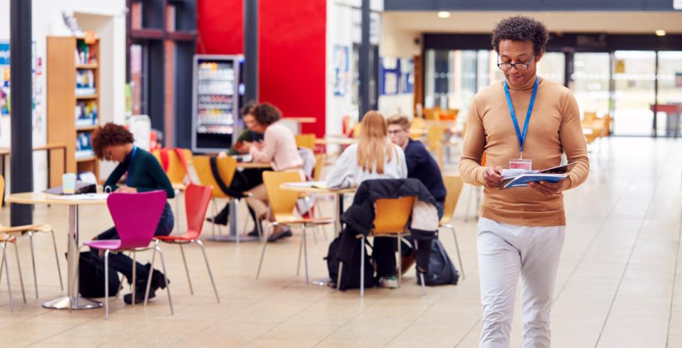 Fellesområde på campus med studenter som sitter ved bordene og jobber og en mann som går