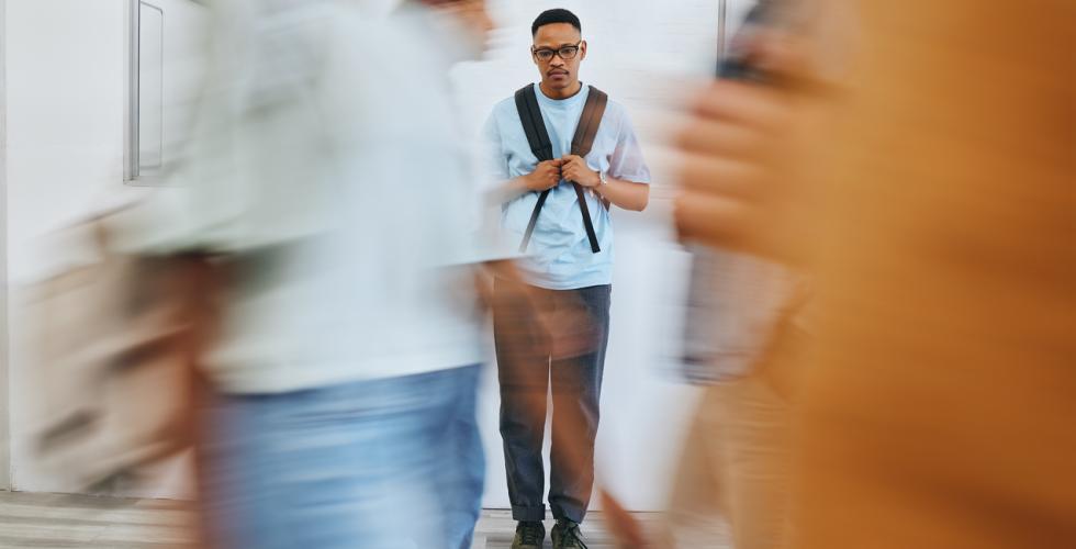En trist mann går i gangen på et universitet omgitt av mange andre mennesker