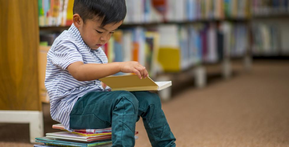 Liten gutt som sitter på en bokstabel og leser 