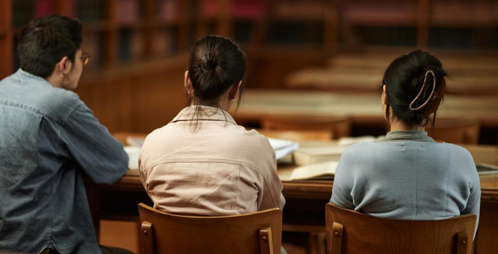 Tre studenter sitter sammen i et bibliotek på campus. 