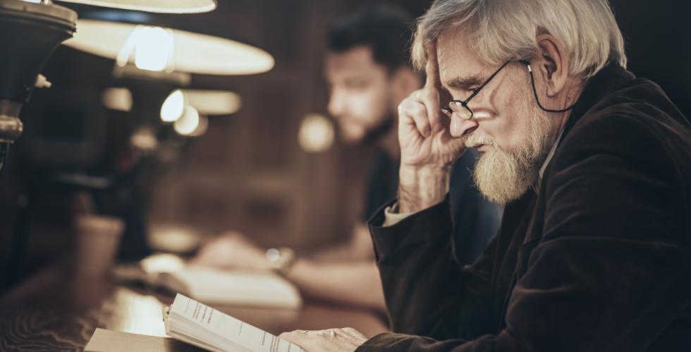 En eldre mann sitter og leser i en bok med flere lesende mennesker i bakgrunnen