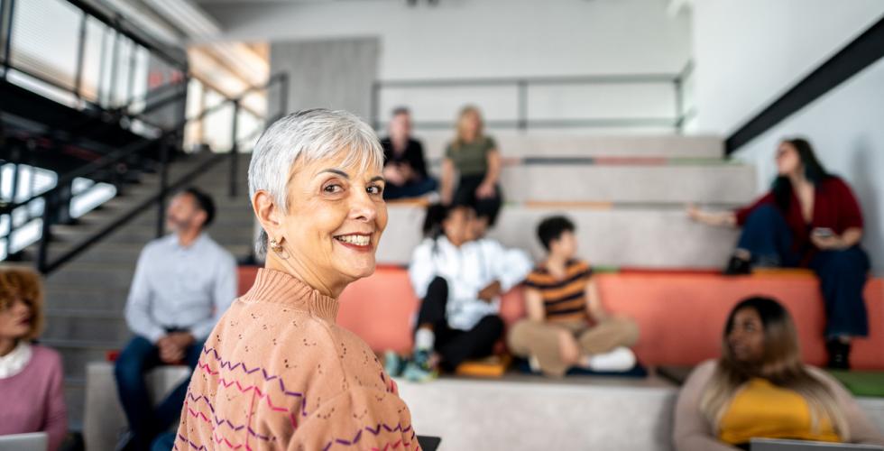 En kvinnelig professor ser mot kamera, mens det sitter flere mennesker i et auditorium