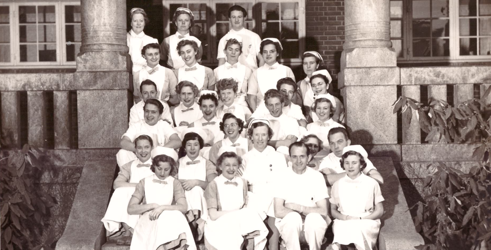 Historisk bilde av mange kvinnelige og sju mannlige ferdig utdannede sykepleiere i Danmark 1954, som sitter ute p&aring; en trapp