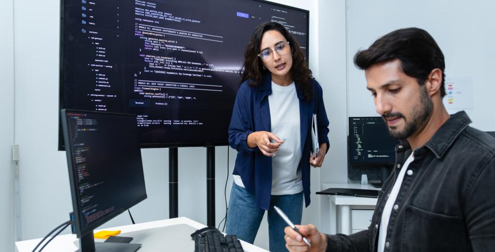En kvinnelig og en mannlig programvareutvikler jobber med store pc-er