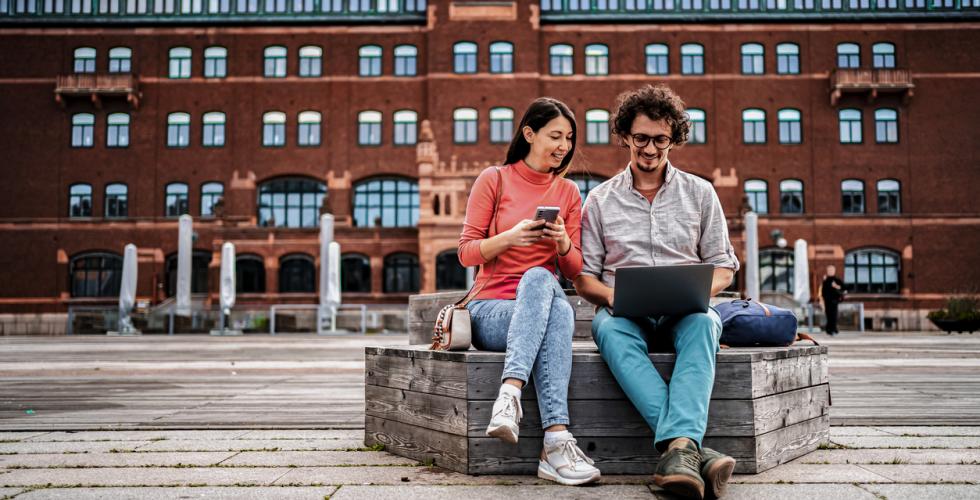 En ung kvinne og en ung mann sitter p&aring; en benk i en storby