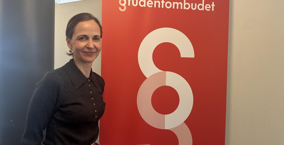 Studentombud Marianne H&oslash;va Rustberggard st&aring;r foran en plakat der det st&aring;r &laquo;Studentombudet&raquo;