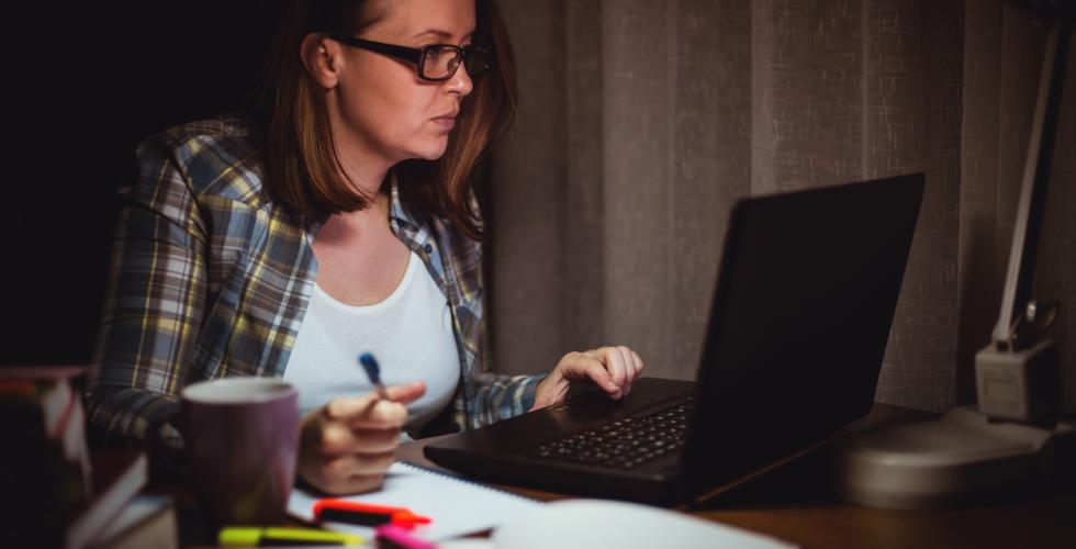 Ung, sliten kvinne jobber sent og sitter ved pc-en hjemmefra 