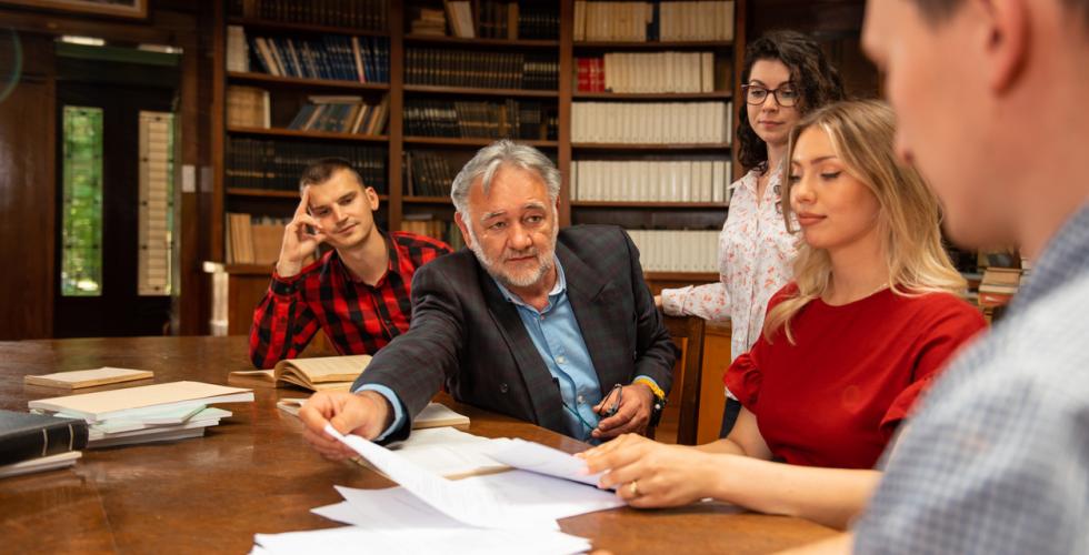 Mannlig professor sitter ved et bord og underviser en gruppe studenter