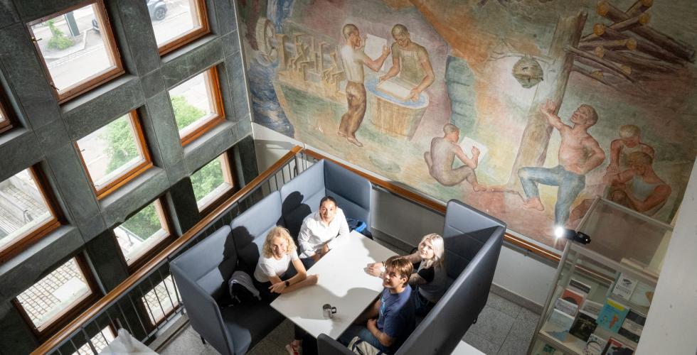 Fire studenter fra Psykologisk institutt ved UiO sitter ved et bord og jobber og ser opp p&aring; fotografen